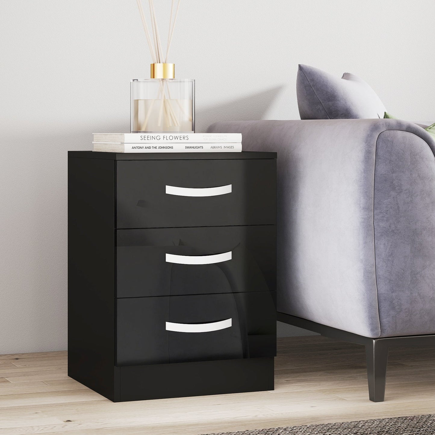 Black nightstand with three drawers next to a gray sofa in a room.